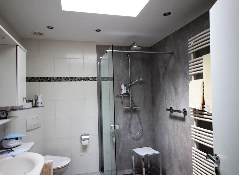 Modernes Badezimmer mit teilgefliester Wand, bodengleicher Dusche und Glasabtrennung. Helle Fliesen und fugenlose Wände in Betonoptik verleihen dem Raum eine stilvolle und funktionale Gestaltung.