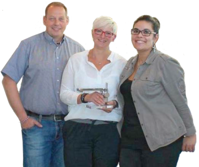 Drei Personen stehen lächelnd zusammen, wobei die Person in der Mitte einen Wasserhahn hält.