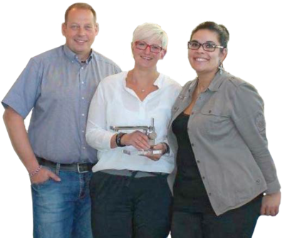 Drei Personen stehen lächelnd zusammen, wobei die Person in der Mitte einen Wasserhahn hält.