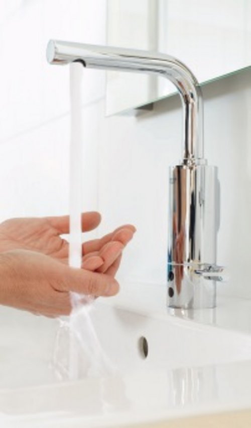 Eine Person wäscht sich die Hände unter einem modernen verchromten Waschbeckenhahn mit fließendem Wasser.