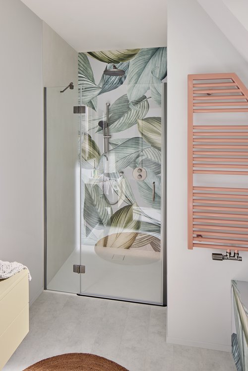 Modernes Badezimmer mit tropischem Flair: Die Dusche wird durch eine großflächige, grüne Blättertapete zum Hingucker. Ein farblich abgestimmter, korallroter Handtuchheizkörper setzt einen stilvollen Akzent.